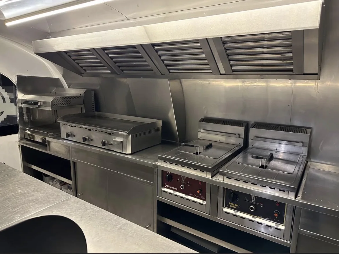 Cuisine de remorque burger équipée d’une plancha et de friteuses sous une hotte d’extraction