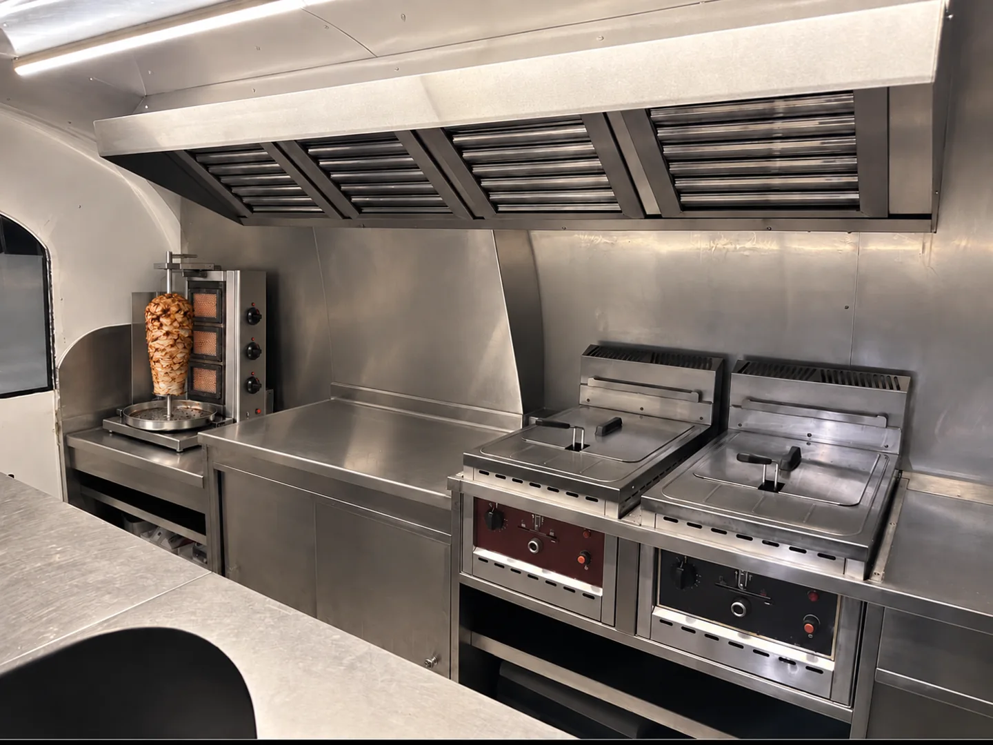 Intérieur inox d’une remorque food truck avec broche à kebab installée au fond à gauche sur un plan rabaissé